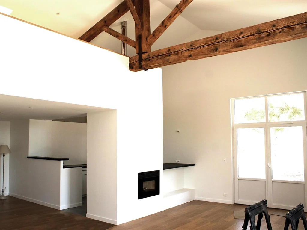 Intérieur réhabilité d'une bâtisse ancienne en loft avec peinture blanche et poutres apparentes par ADS Rénovation à Valbonne