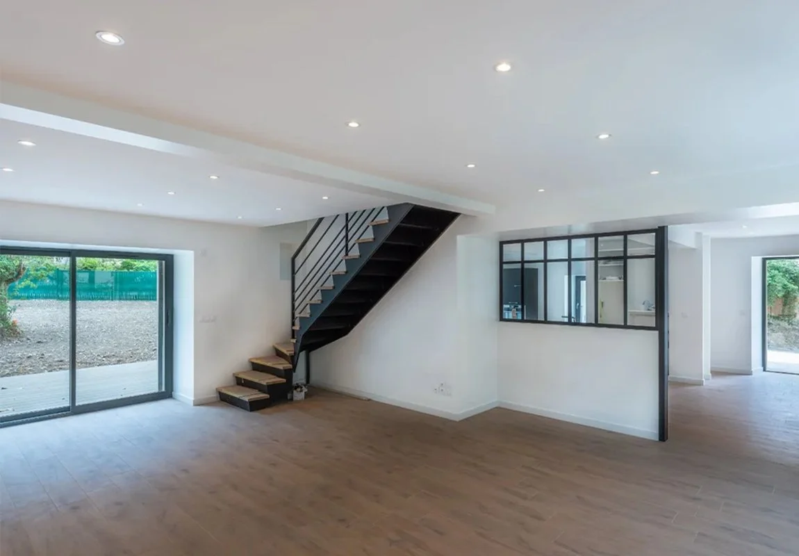 Résultat d'une rénovation complète de villa par ADS Rénovation à Cannes — salon lumineux avec escalier métallique, verrière et baies vitrées sur jardin