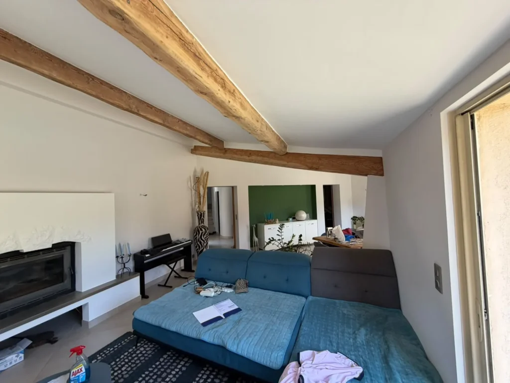 Salon rénové avec poutres en bois apparentes, canapé bleu et cheminée